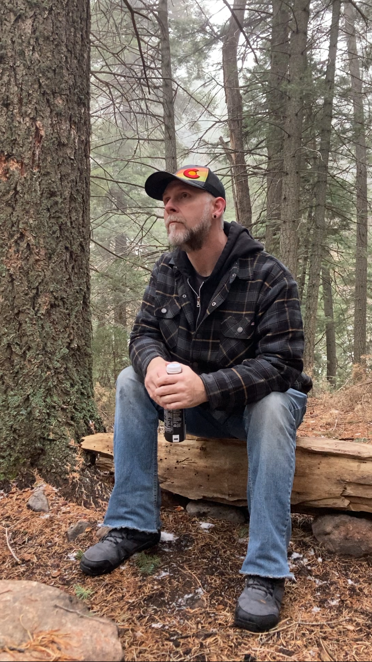 Justin Whedon seated on a log in a Colorado forest